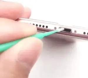 Person cleaning a phone’s charging port to remove dust and fix phone charger
