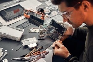 Technician inspecting and repairing a smartphone on a workbench to diagnose charging issues.
